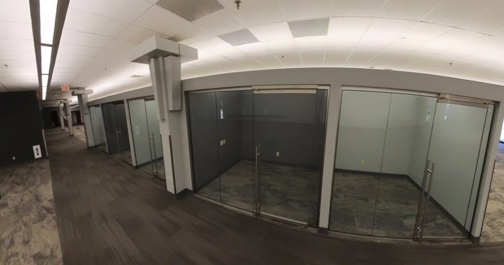 A modern office hallway at 3281 Armar Drive features several empty glass-walled offices, gray carpet, and white ceiling tiles.