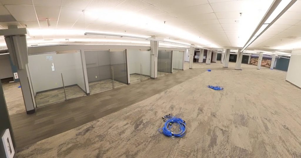 Empty office space at 3281 Armar Drive with glass-walled cubicles, exposed ceiling lights, and several coils of blue network cables on the carpeted floor.