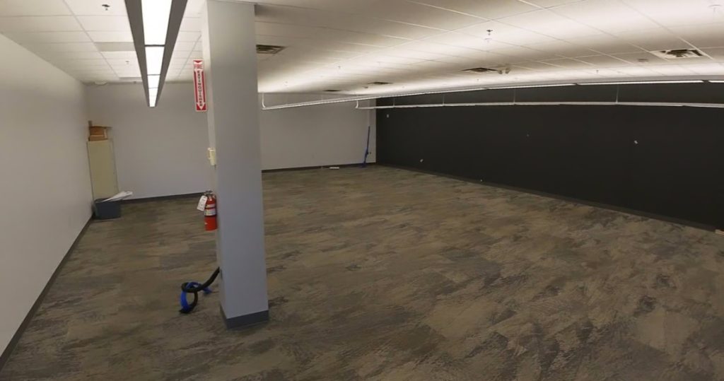 A large, empty office space at 3281 Armar Drive features gray carpet, white walls, a black accent wall, fire extinguisher, vacuum cleaner, and ceiling lights.
