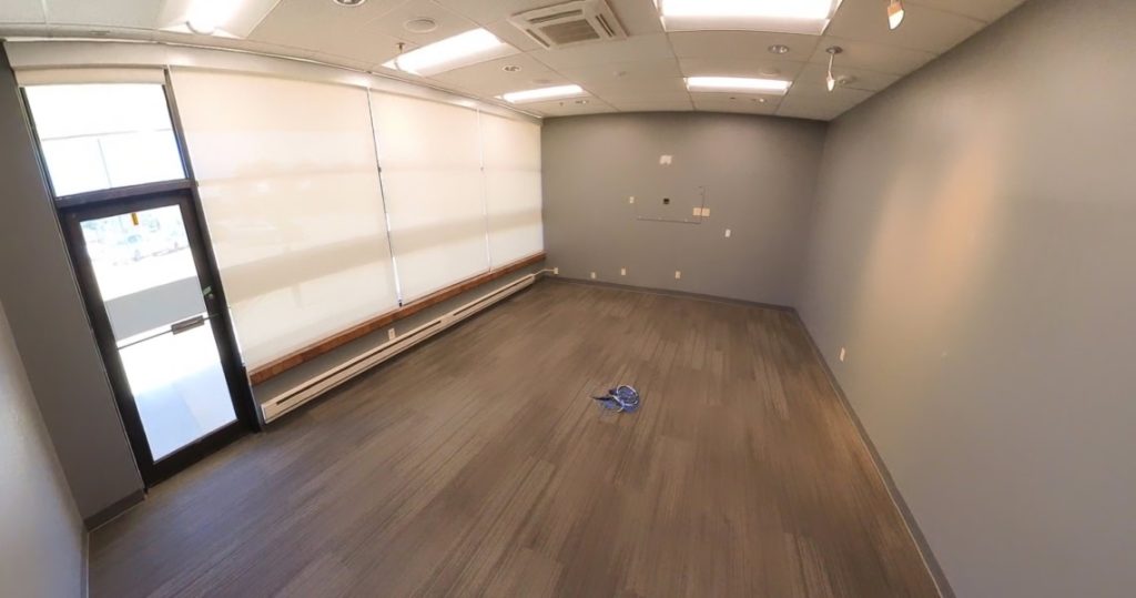 Empty office room at 3281 Armar Drive with gray walls and floor, large covered windows, overhead lights, and a small bundle of blue cables on the floor.