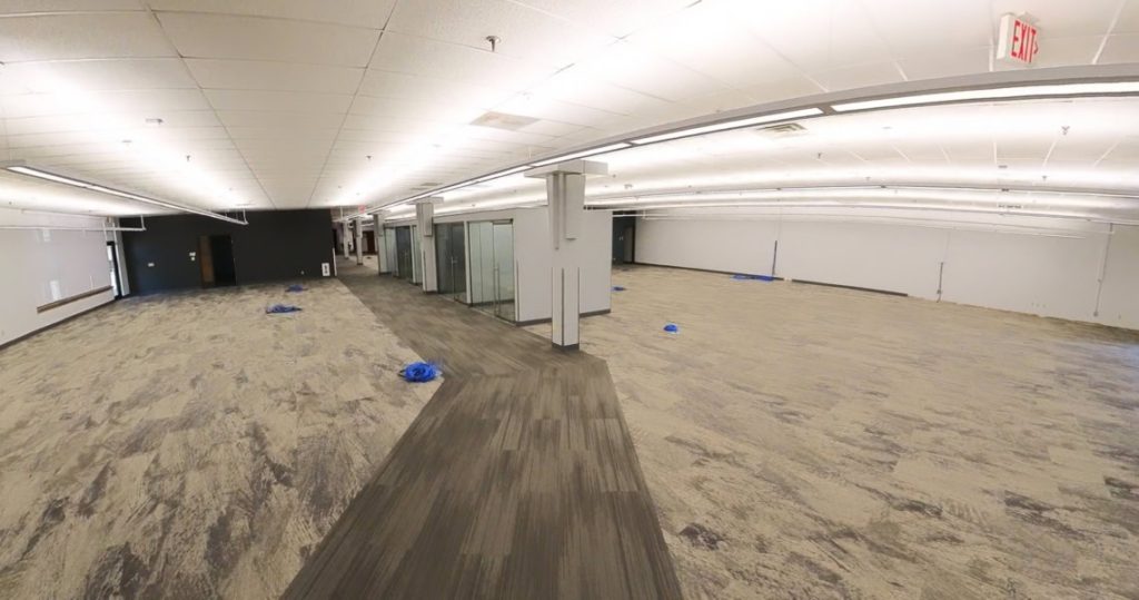 A large, mostly empty office space at 3281 Armar Drive features overhead fluorescent lighting, glass-walled rooms, and scattered blue plastic coverings on the carpeted floor.
