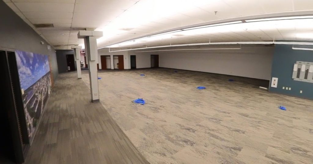 A large, mostly empty office space at 3281 Armar Drive features gray carpet, a mural on one wall, and several blue cables laid out on the floor.