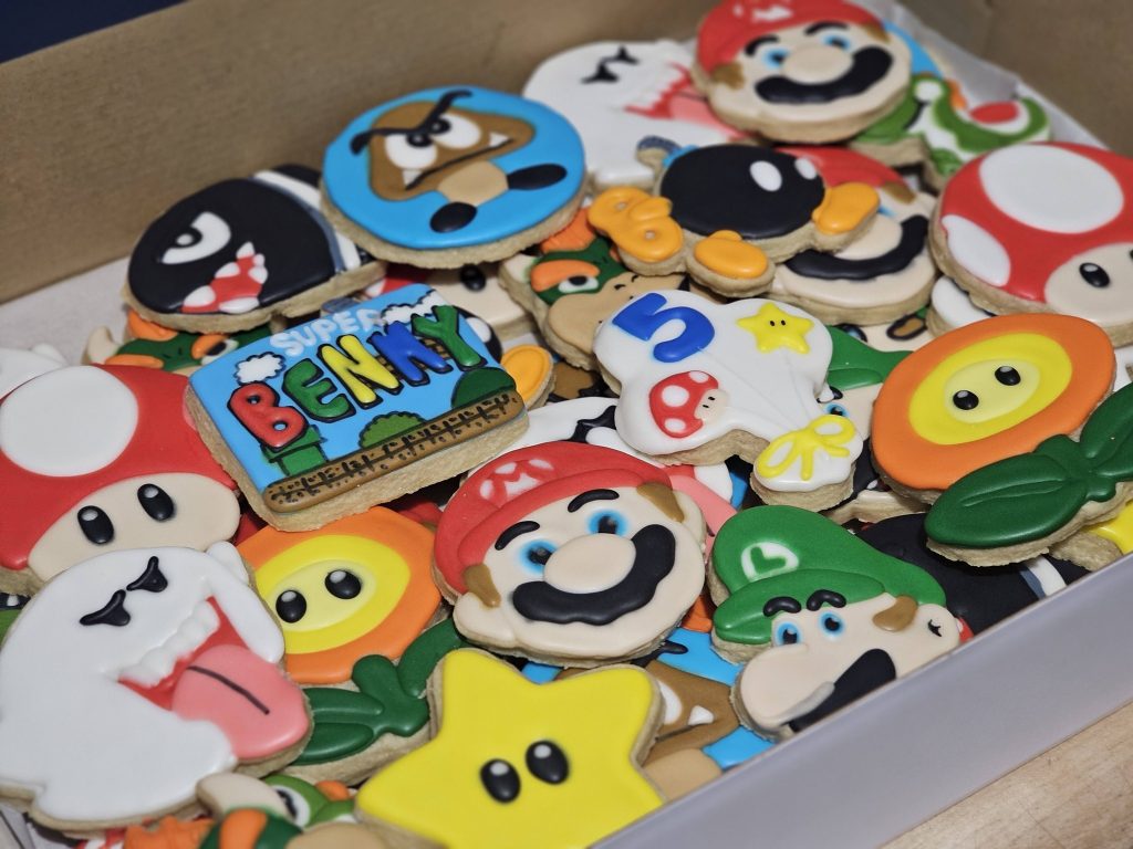 A box filled with decorated sugar cookies featuring characters and symbols from the Super Mario video game series, freshly made by KC Cakes in Cedar Rapids.