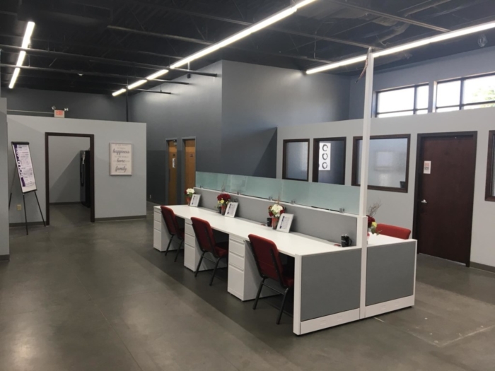 A modern office space by Keller Williams Realty featuring four workstations, red chairs, and gray partitions. Closed doors surround the area, while wall art and framed items add character—perfect for our latest Tenant Spotlight.
