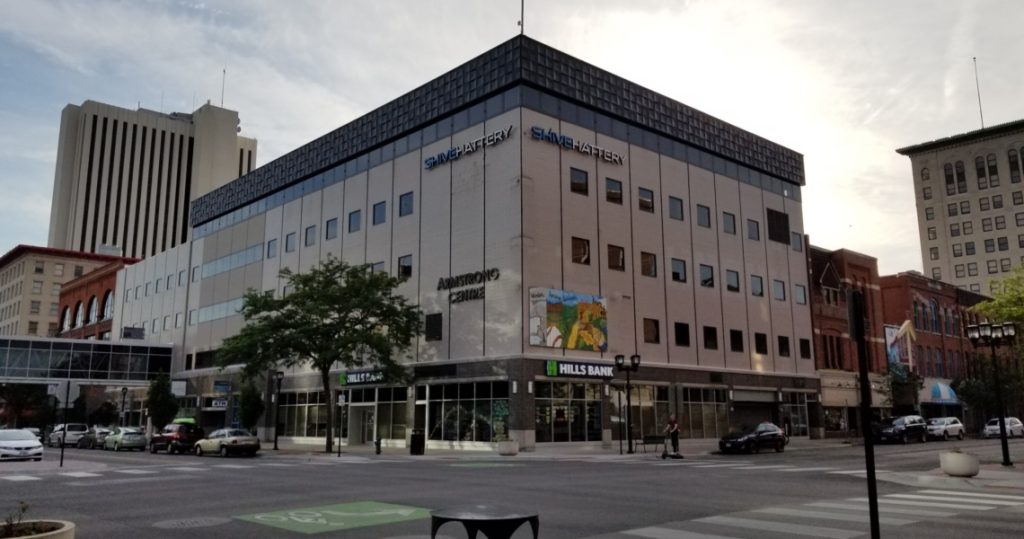 A four-story office building labeled Armstrong Centre and SHIVE-HATTERY stands on a city street corner, surrounded by businesses and parked cars.