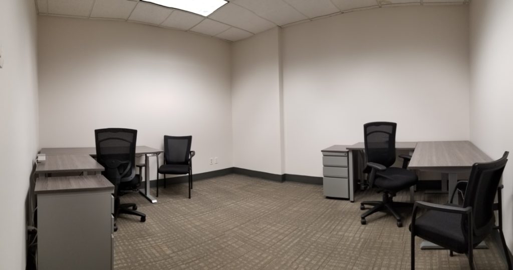 Empty office room with three desks, three office chairs, and a neutral color scheme. Overhead lights are on, and there are no decorations or windows visible—ideal for those seeking professional space through Armstrong Office Suites office rentals.