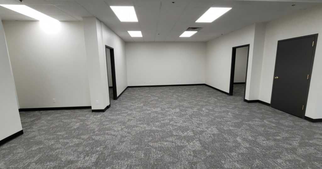 Empty office room in the Granby Building, Suite 200, with gray carpet, white walls, overhead fluorescent lights, and three black doors.
